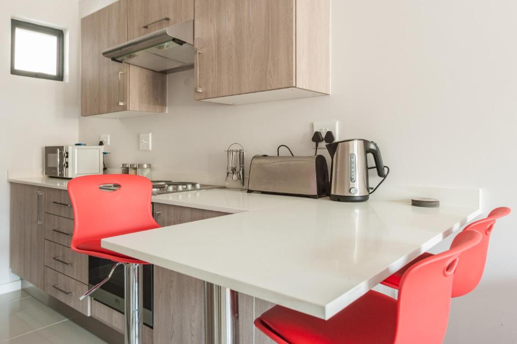 uma cozinha com um balcão branco e cadeiras vermelhas em The Rand Haven em Midrand
