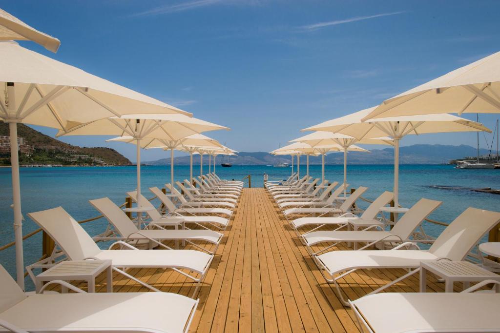 a row of white chairs and umbrellas on a dock at Bellazure Hotel in Akyarlar