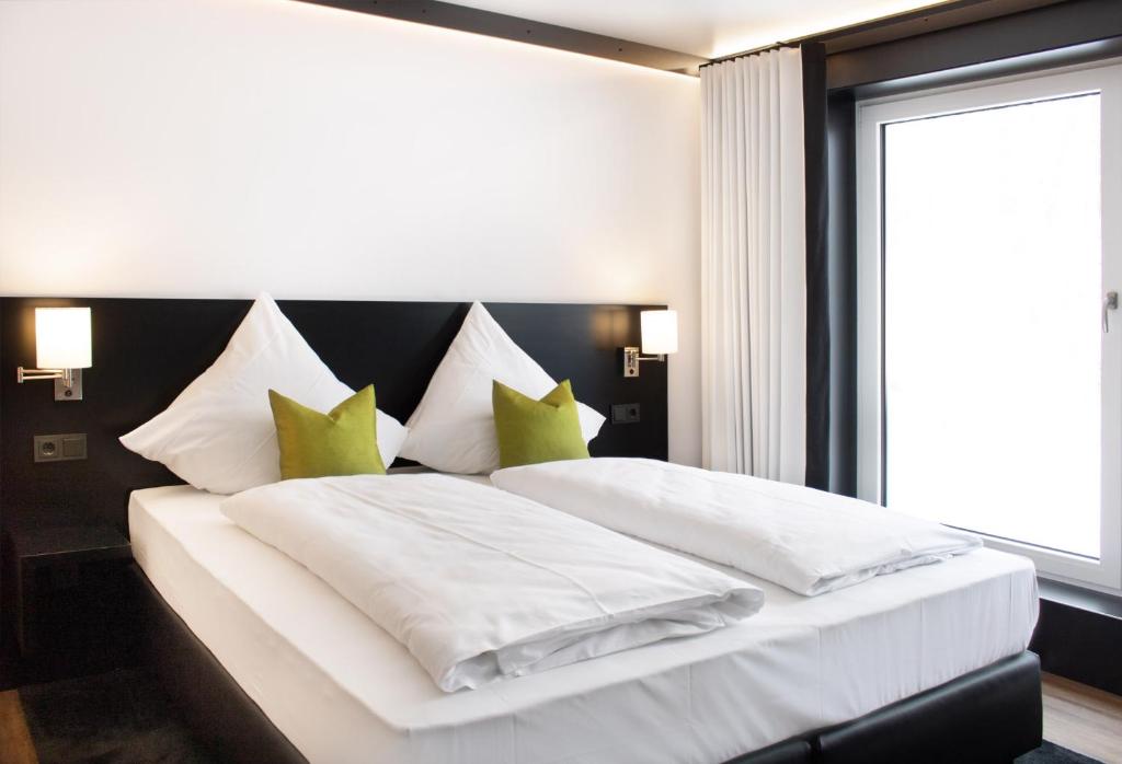 um quarto com uma grande cama branca com almofadas verdes em DO Hotel by WMM Hotels em Dornstadt