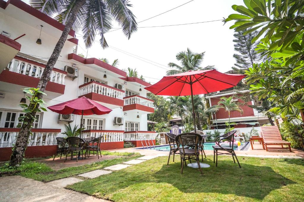 a patio with tables and chairs and a red umbrella at Grande Ave Maria Resort in Candolim