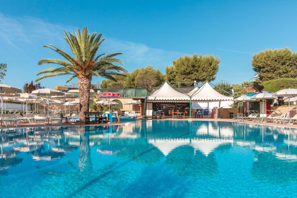 a large swimming pool with a palm tree and tents at Residence Camping Atlantide in Monopoli