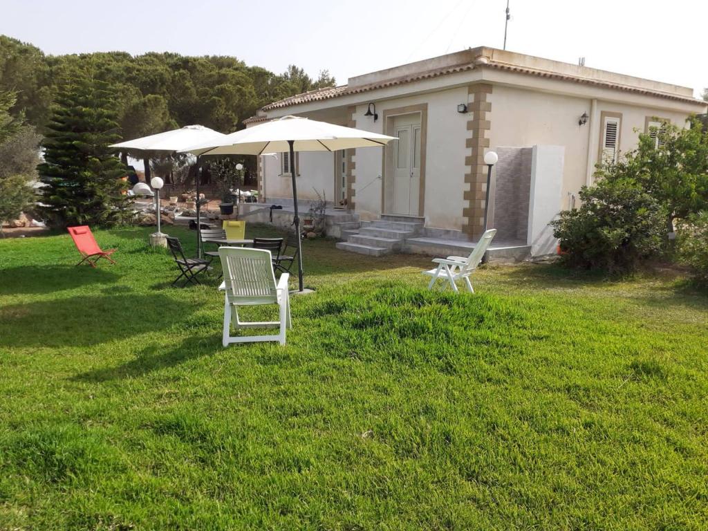 einen Garten mit Stühlen und einem Regenschirm und einem Haus in der Unterkunft Bilocale Conca in villa climatizzata - Wi-fi in pieno rekax in Marzamemi