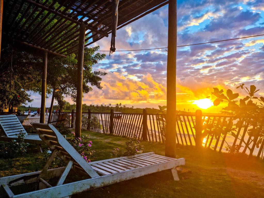 a porch with a bench and the sunset in the background at Pousada Pérola do Atlântico in Ilha de Boipeba