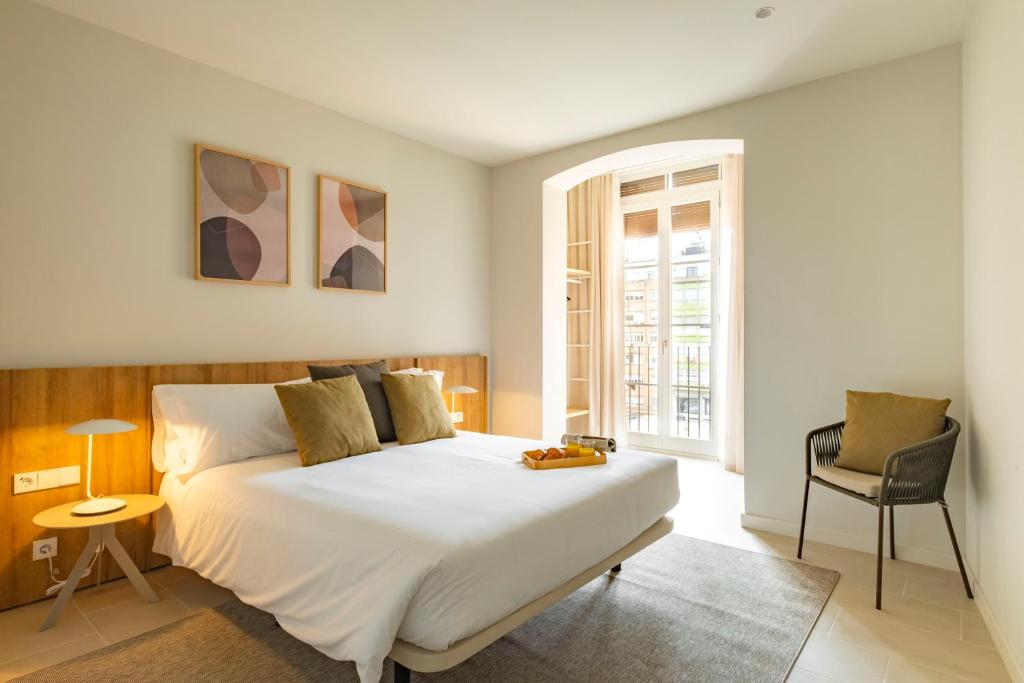 ein Schlafzimmer mit einem großen weißen Bett und einem Stuhl in der Unterkunft Aspasios Garden Apartments in Barcelona