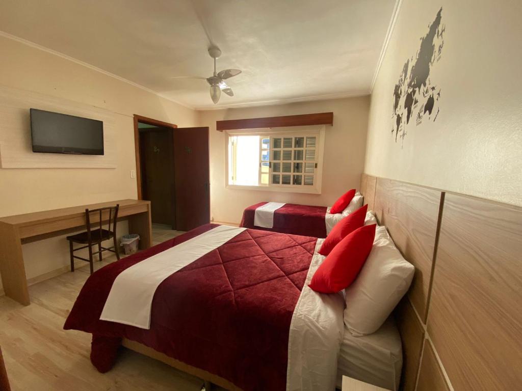 Schlafzimmer mit einem Bett mit roten Kissen und einem Schreibtisch in der Unterkunft Casa do Rogerio Hostel - Unidade Shopping in Caxias do Sul