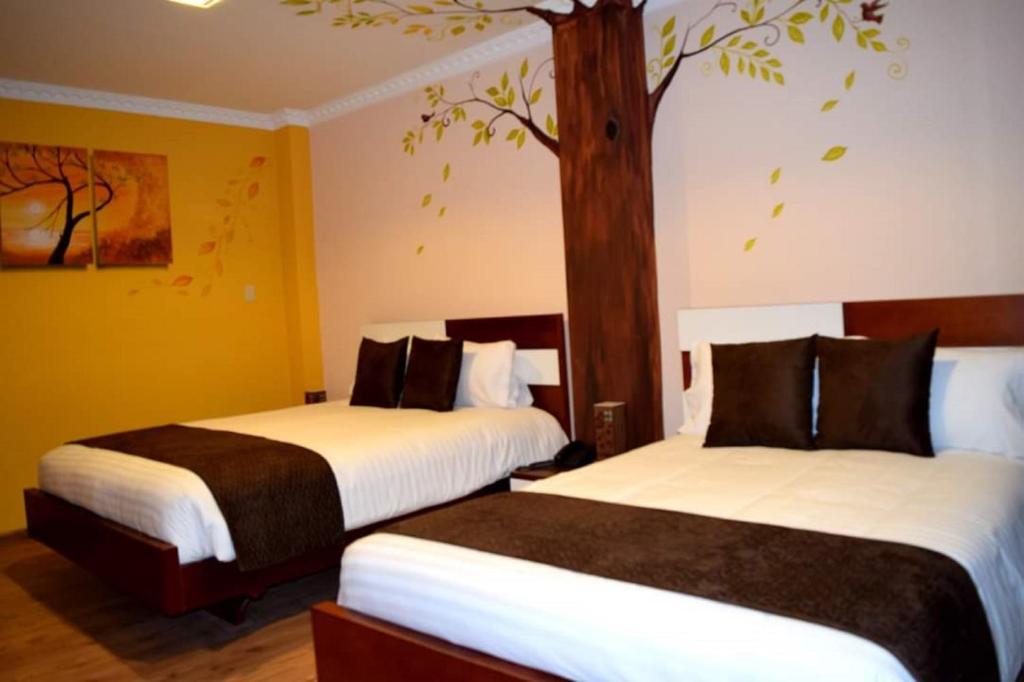 Dos camas en una habitación de hotel con un árbol en la pared. en La Kapital Hotel, en Ambato