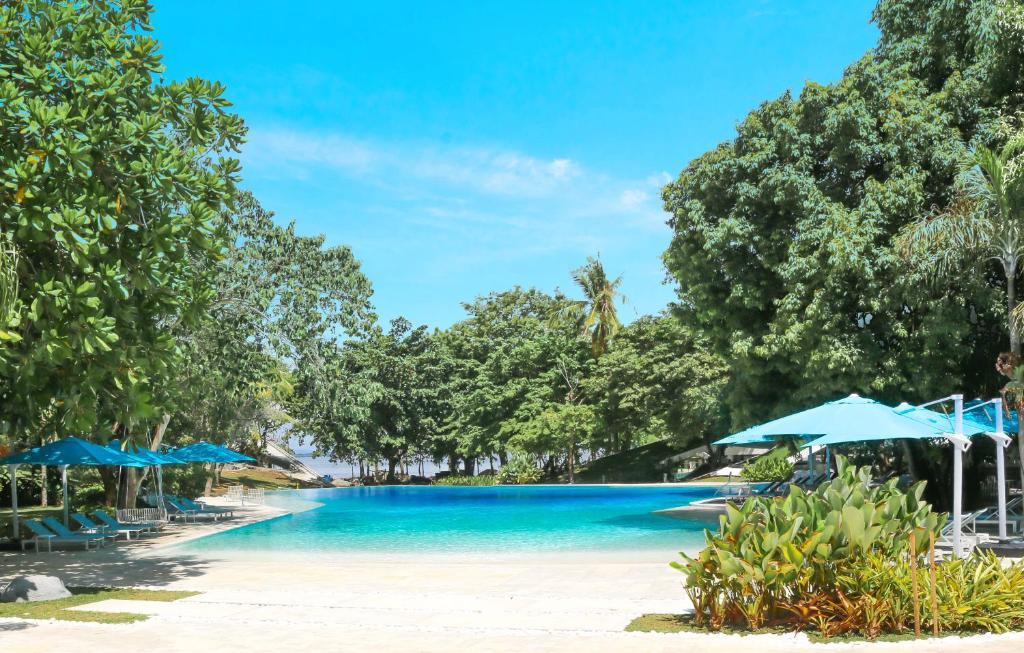 a swimming pool with blue umbrellas on a beach at Tambuli Seaside Resort and Spa in Mactan