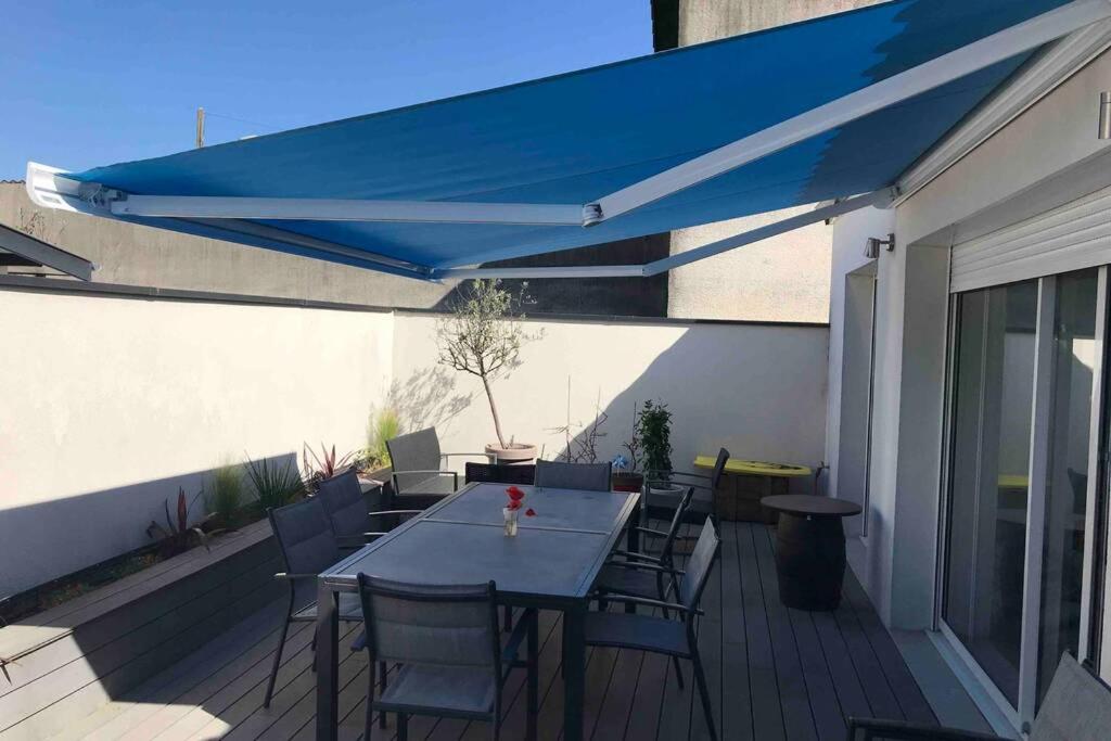 een patio met een tafel en stoelen en een blauwe parasol bij Maison lumineuse 3 chambres bordeaux sud in Pont-de-la-Maye