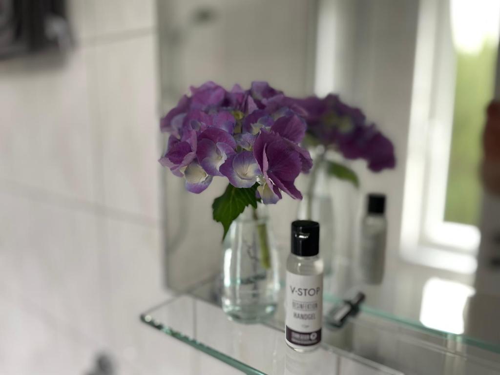 a vase of purple flowers on a counter with a bottle of moisturizers at Apartment Oesterling in Wardenburg