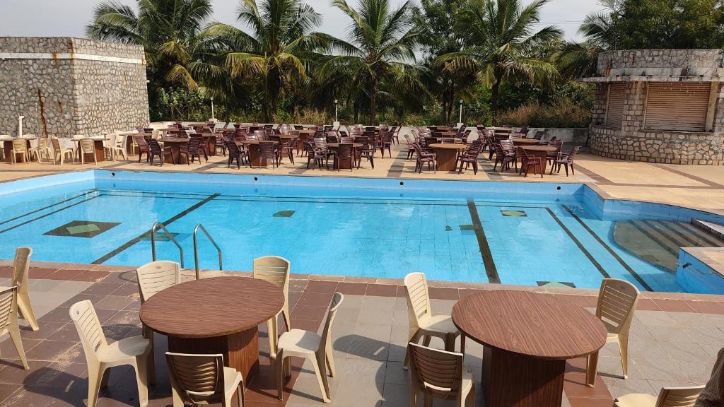 Kanthi Resorts Badami في Bāgalkot: مسبح بالطاولات والكراسي بجانب مطعم