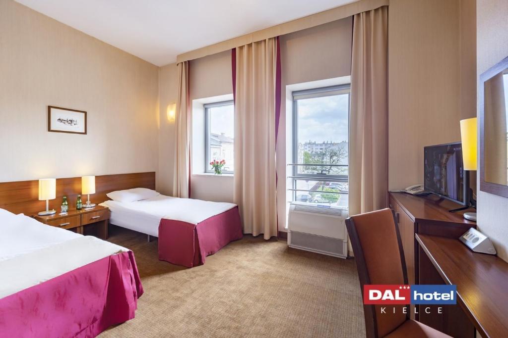 Twin hotel room with two single beds, bedside lamps, desk, two windows, light neutral décor.