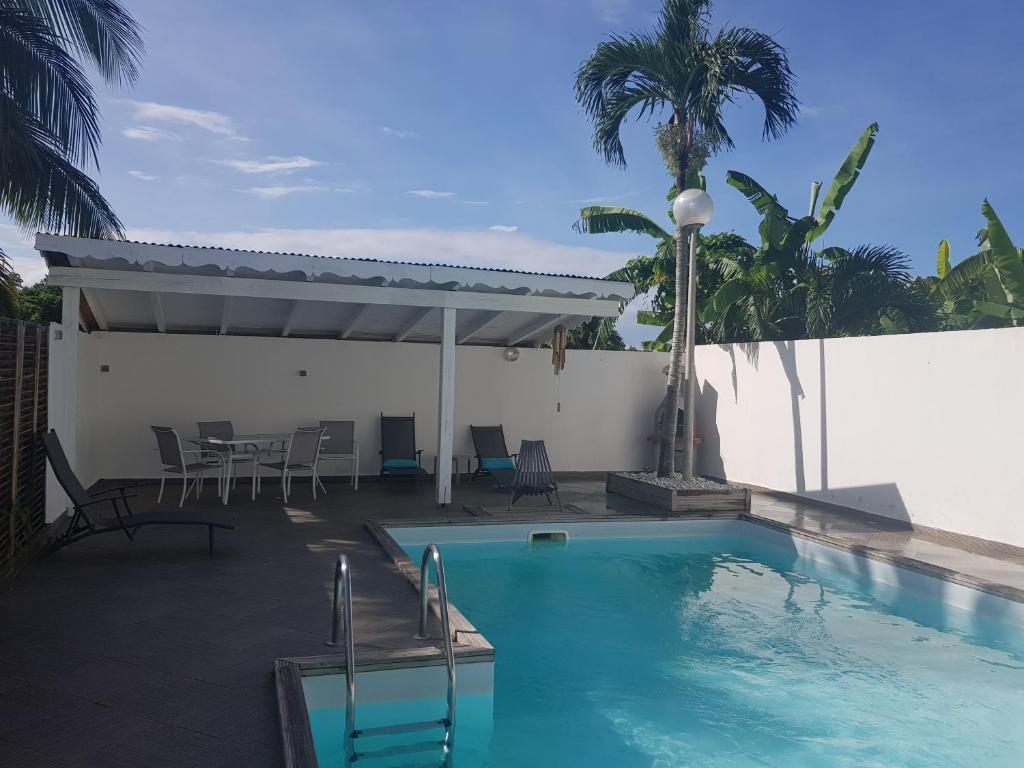 a swimming pool with a table and chairs next to a white wall at Gîte Akwarel in Vieux-Habitants