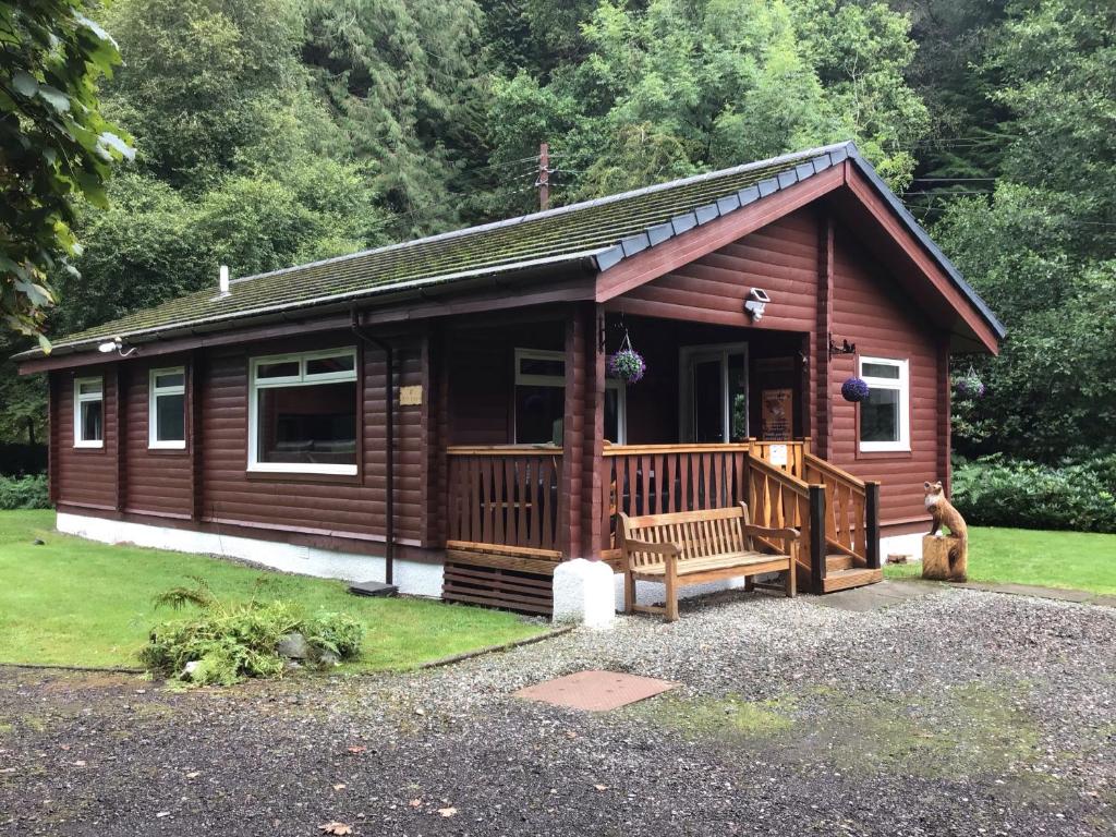 Cabaña de madera grande con banco en un patio en Fox Lodge Traditional Log Cabin en Dunoon