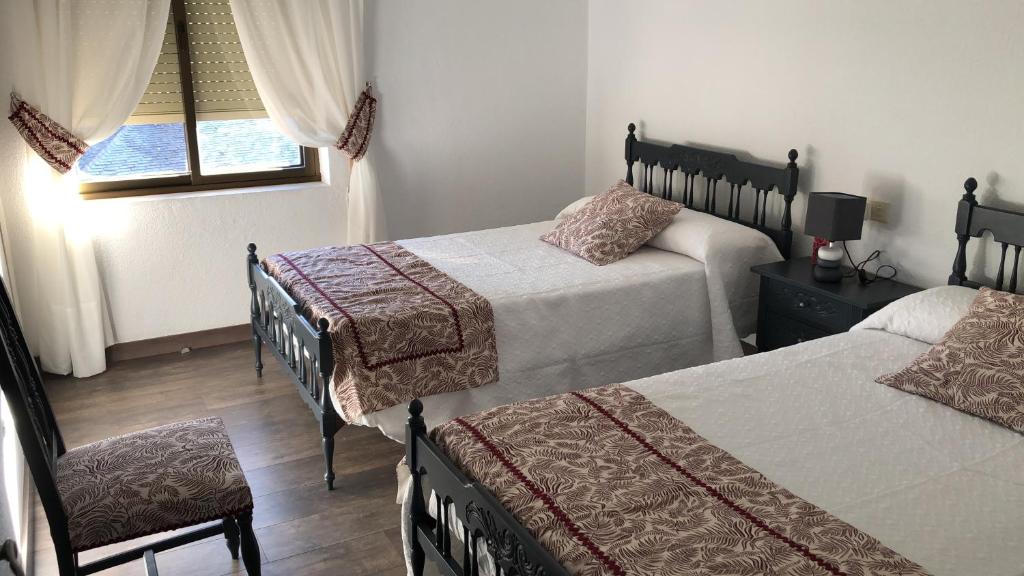 a bedroom with two beds and a chair and a window at El Mirador de la Villa in Puebla de Sanabria