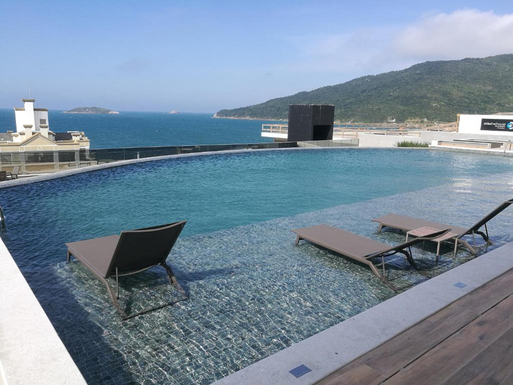 una piscina con due sedie e l'oceano di EA-Apto com vista do mar em Praia dos Ingleses a Florianópolis