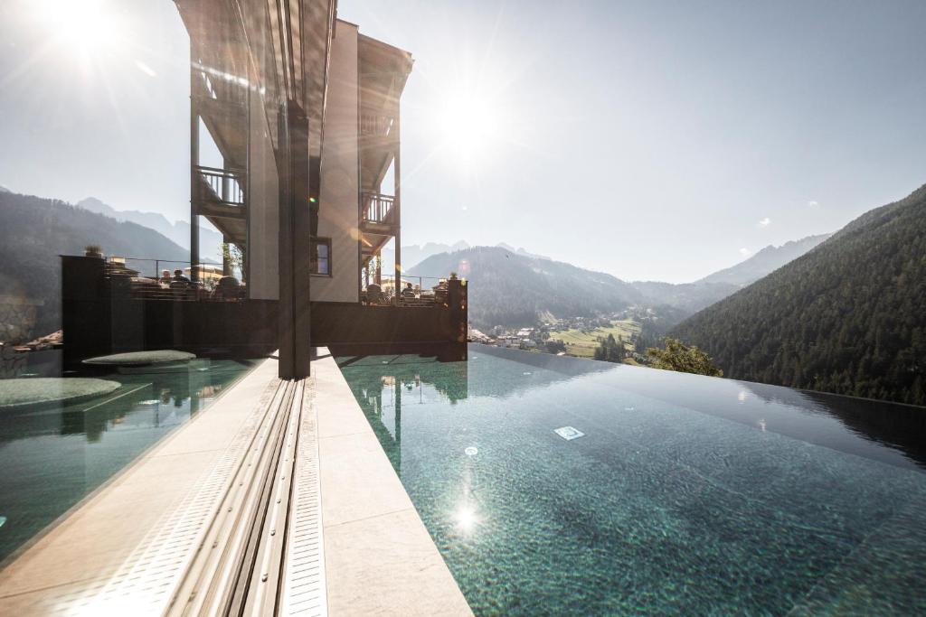 um hotel com uma piscina de beiral infinito com montanhas ao fundo em Charme Hotel Friedrich em Nova Levante