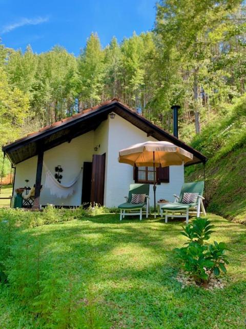 a small house with two chairs and an umbrella at Chalé de luxo pertinho de Monte Verde in Monte Verde