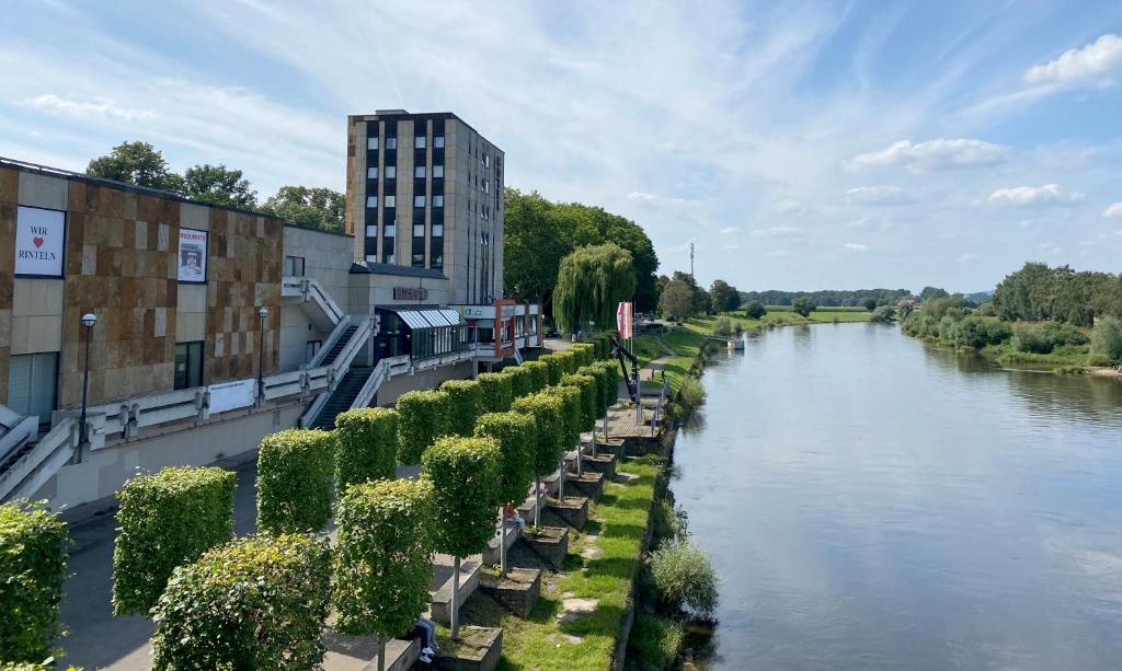 ein Fluss mit einer Reihe von Bäumen neben einem Gebäude in der Unterkunft Hotel Brückentor in Rinteln