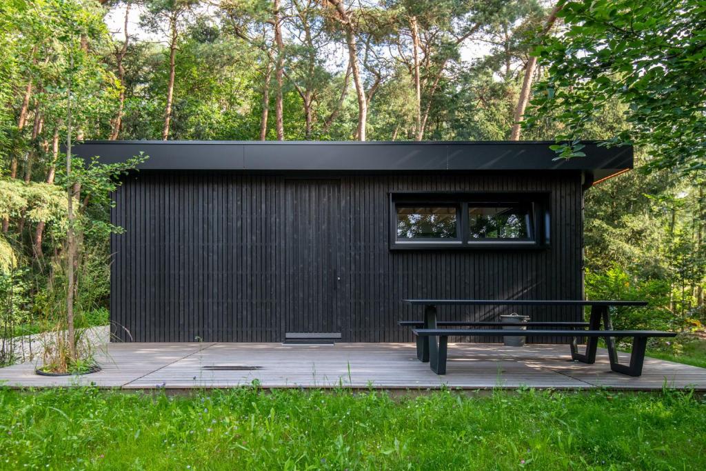 un bâtiment noir avec un banc et une fenêtre dans l'établissement Het Uilennest, à Otterlo