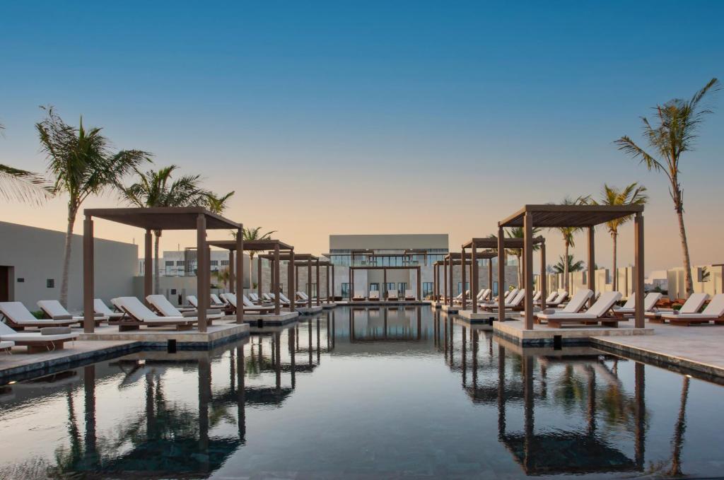 - une piscine avec des chaises longues et des palmiers dans l'établissement Alila Hinu Bay Salalah Mirbat, à Salalah