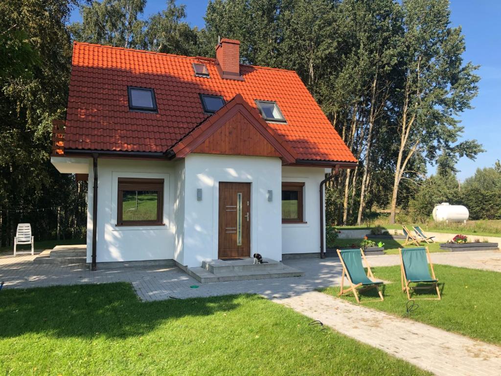 a small white house with an orange roof and two chairs at Caloroczny domek letniskowy ze stawem in Harsz