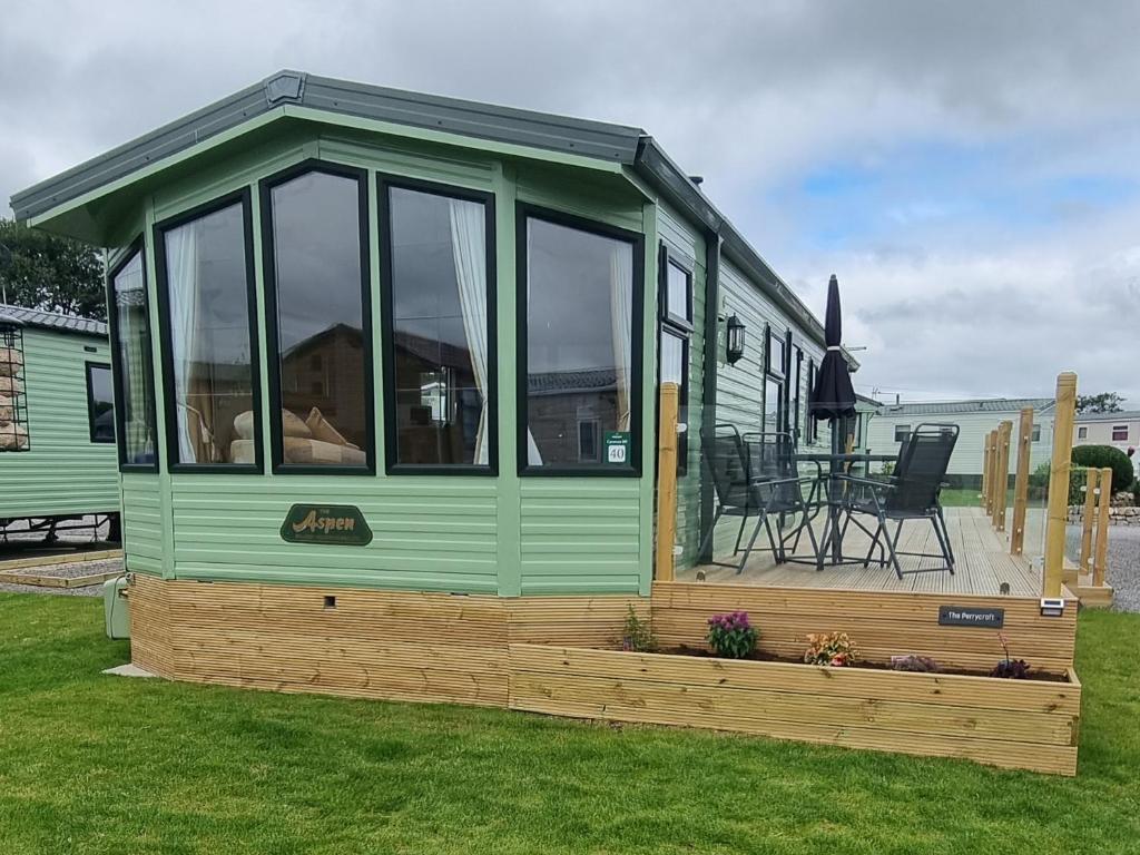 a green tiny house on a deck with a table at The Perrycroft at Forest Views Caravan Park in Plumbland