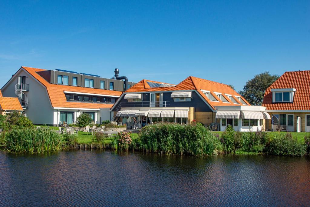 un bâtiment avec des toits orange à côté d'une nappe d'eau dans l'établissement Landgoed Hotel Tatenhove Texel, à De Koog
