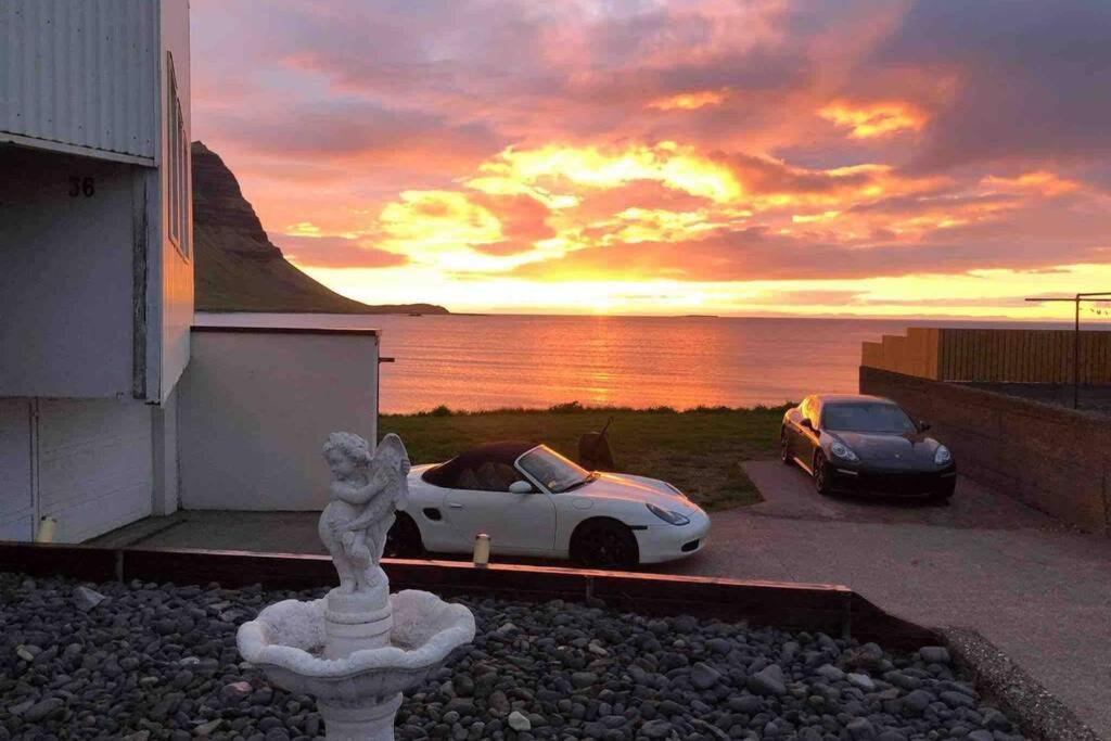 two cars parked outside of a house with a sunset at Kirkjufell Oceanfront Villa in Grundarfjordur