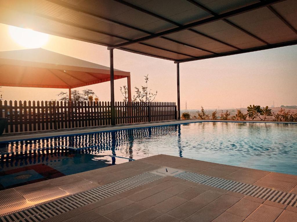 a large swimming pool with a fence and the sun setting at Desert Dune Farmhouse - By Seven Elements in Ras al Khaimah