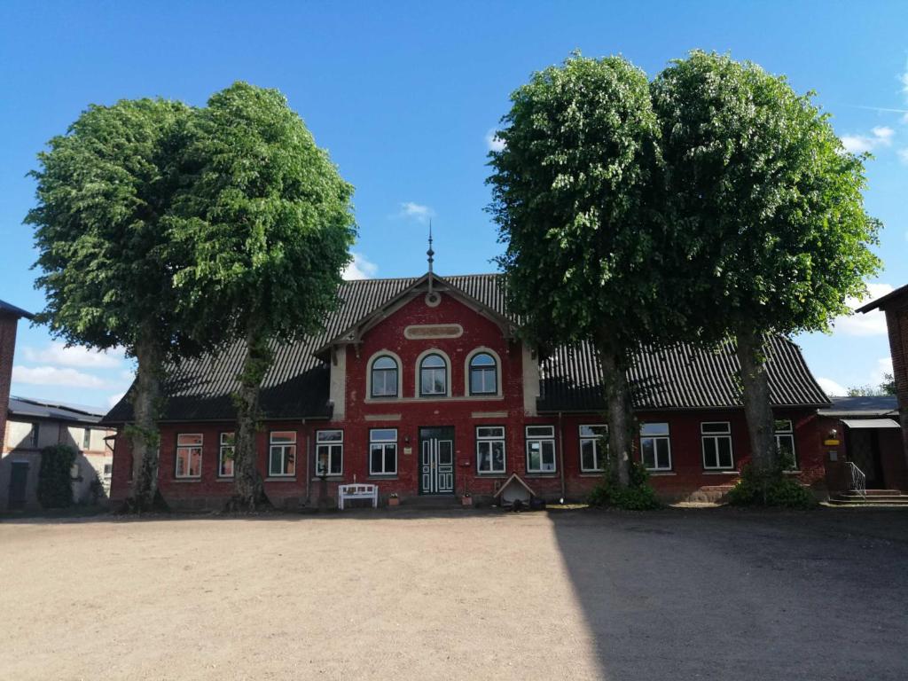 un bâtiment rouge avec deux arbres devant lui dans l'établissement Ferienwohnung Landoase, à Kollerup