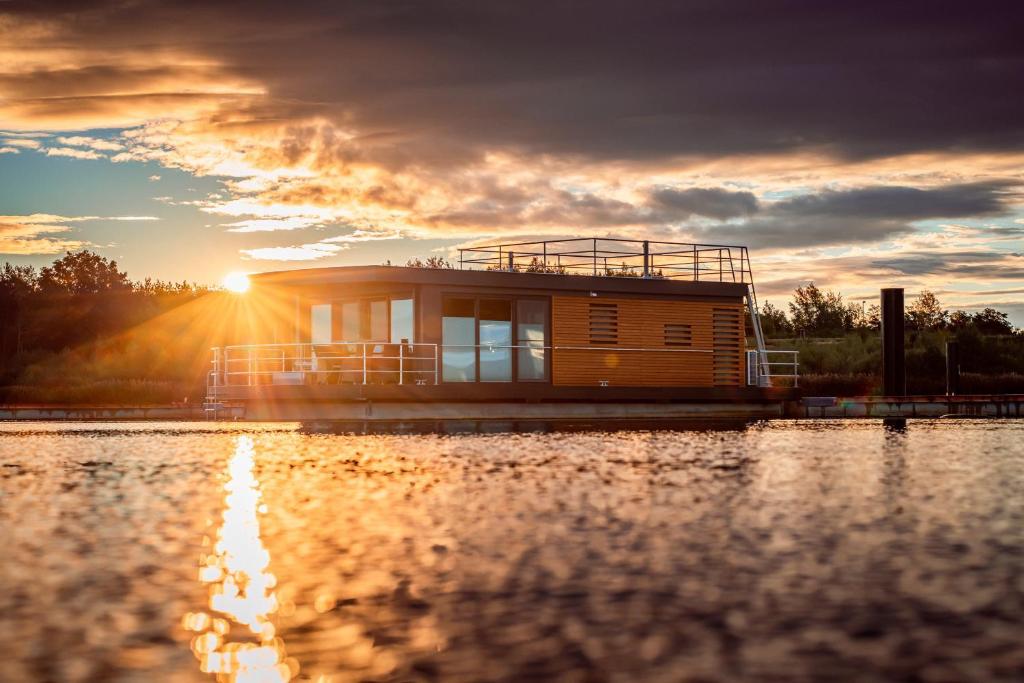ein Haus auf einem Boot im Wasser bei Sonnenuntergang in der Unterkunft Floatinghouses Bärwalder See in Klitten