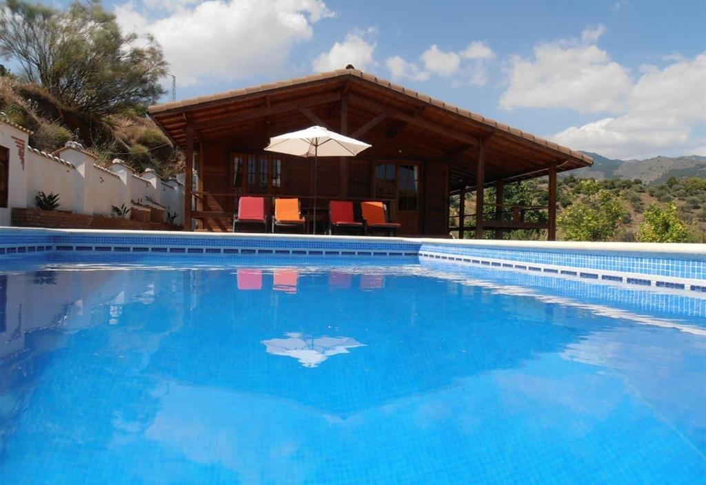 una piscina con una casa y una sombrilla en Casa de Madera, en Sedella