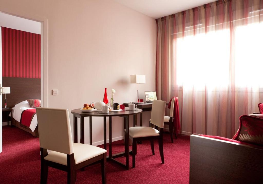 Cette chambre comprend une table, des chaises et un lit. dans l'établissement The Originals Residence KOSY appart'hôtels - Les Cèdres, à Grenoble