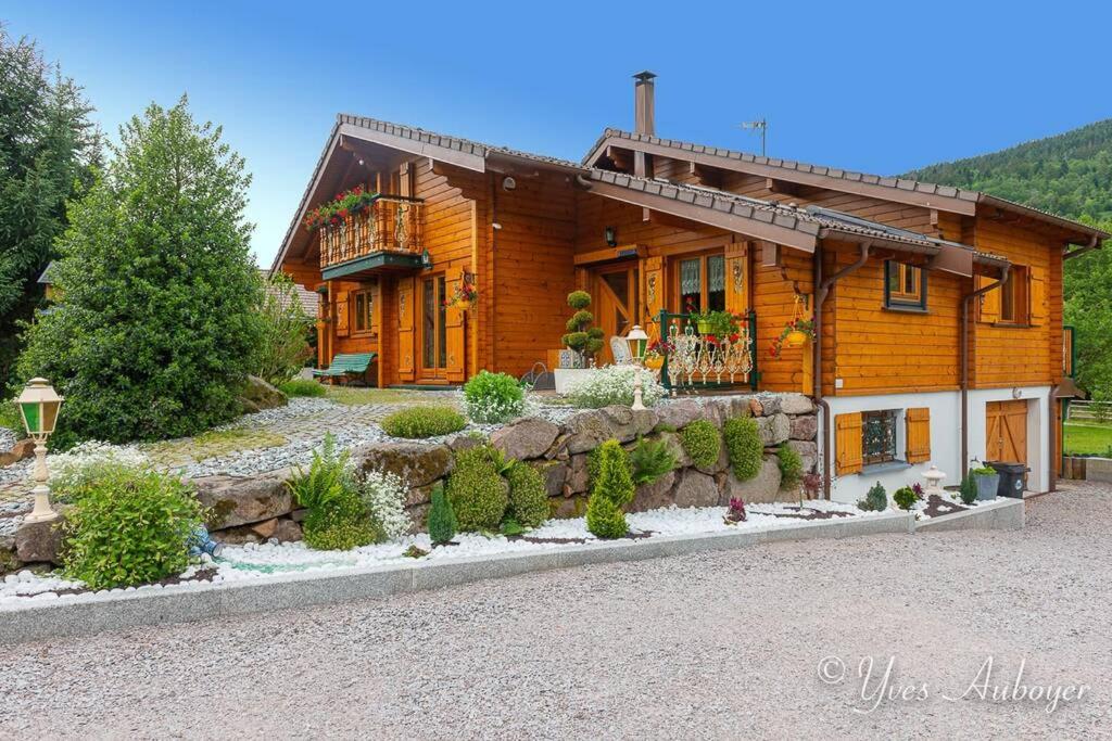 a log house with a stone retaining wall in front of it at Chalet La Revoyotte in Le Ménil