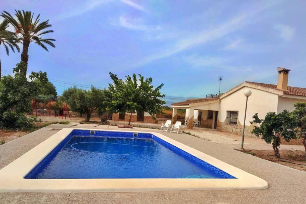 a swimming pool in front of a house at Villa rústica privada con gran chalet y piscina in Elche