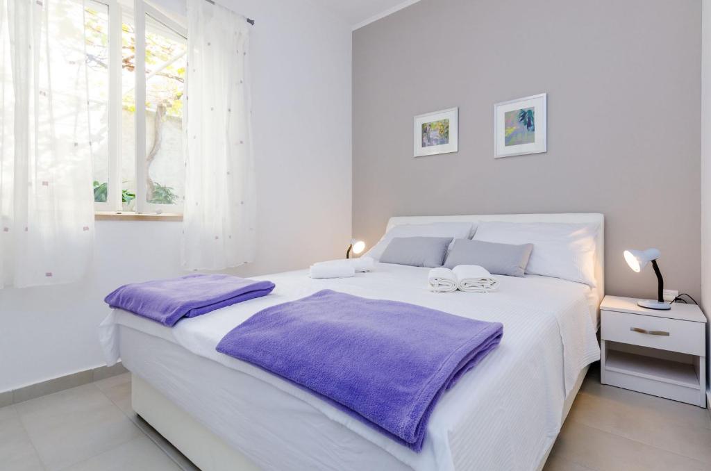 a white bedroom with a large white bed with purple sheets at Rooms Batina in Dubrovnik