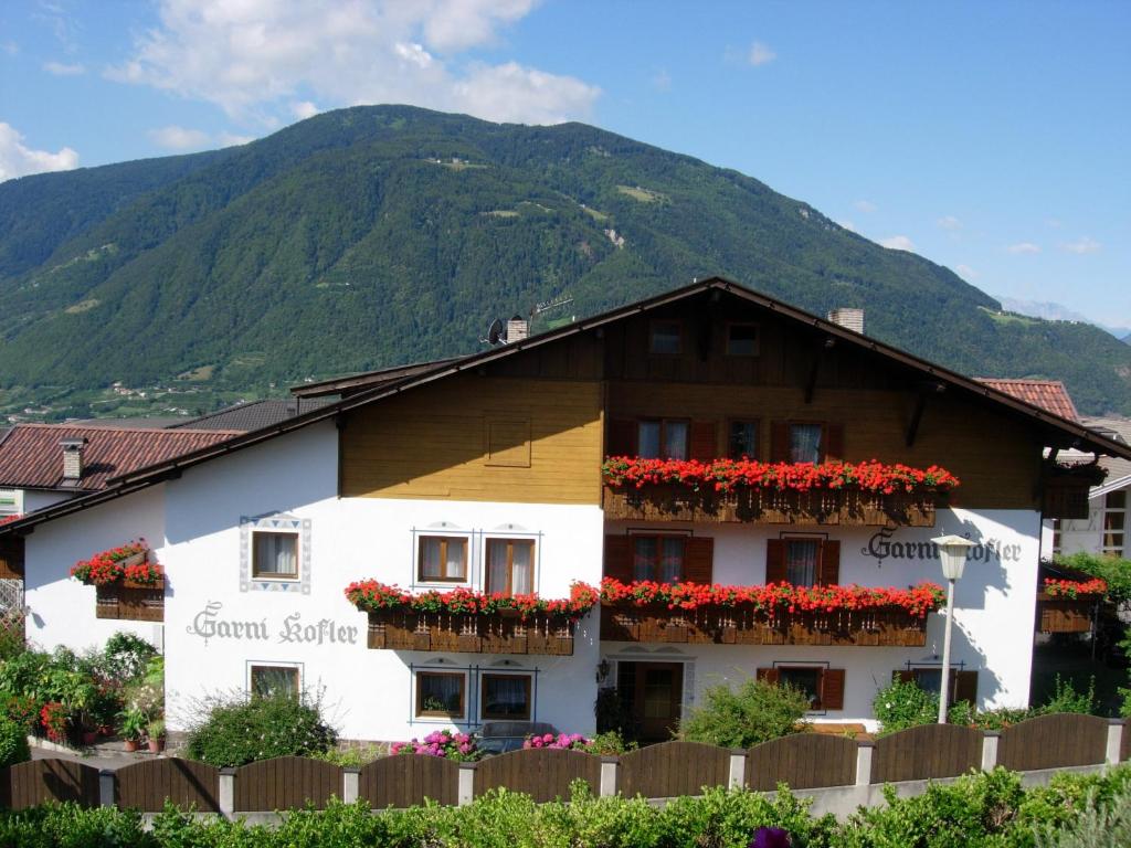 a building with flowers on the windows and a mountain at Garni Kofler in Tirolo