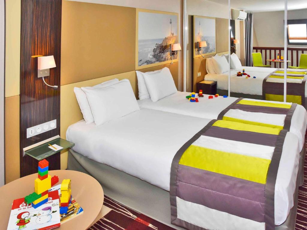 a hotel room with two beds and a table with a table at Mercure Granville Le Grand Large in Granville
