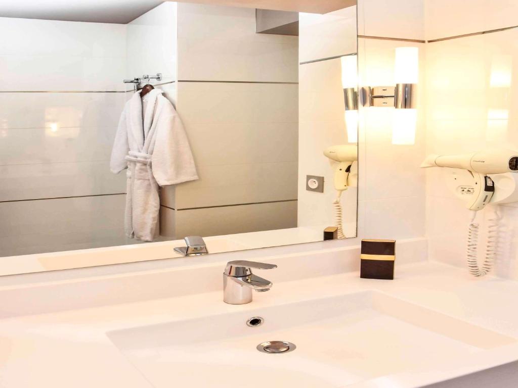 a white bathroom with a sink and a mirror at Mercure Granville Le Grand Large in Granville