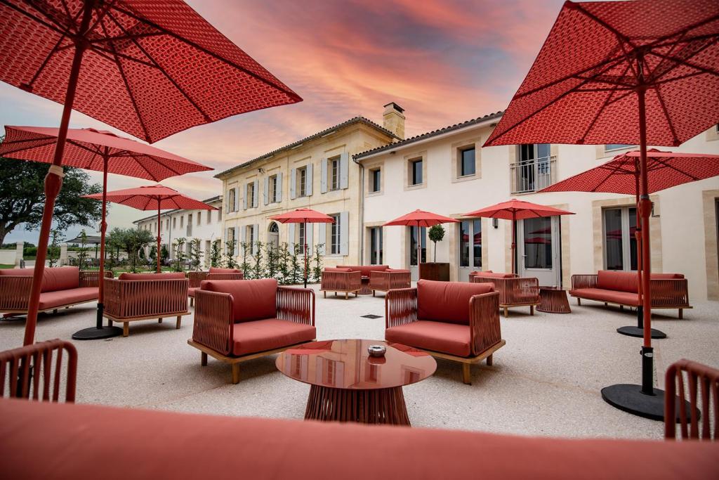 eine Terrasse mit roten Stühlen, Tischen und Sonnenschirmen in der Unterkunft Château Fage La Maison des Vignes - Groupe Teritoria in Arveyres