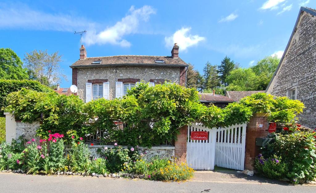 una casa de ladrillo con una valla blanca y flores en Le petit nid d'aigle - Giverny en Giverny