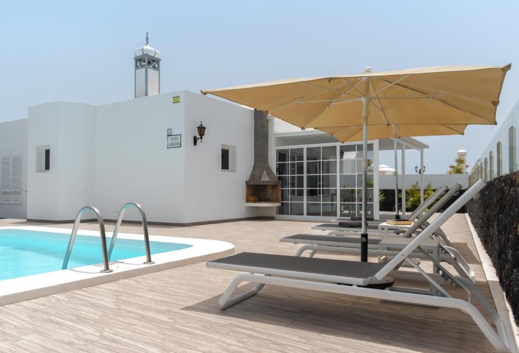 eine Terrasse mit Stühlen und einem Sonnenschirm neben einem Pool in der Unterkunft Villas Maribel Pocillos in Puerto del Carmen