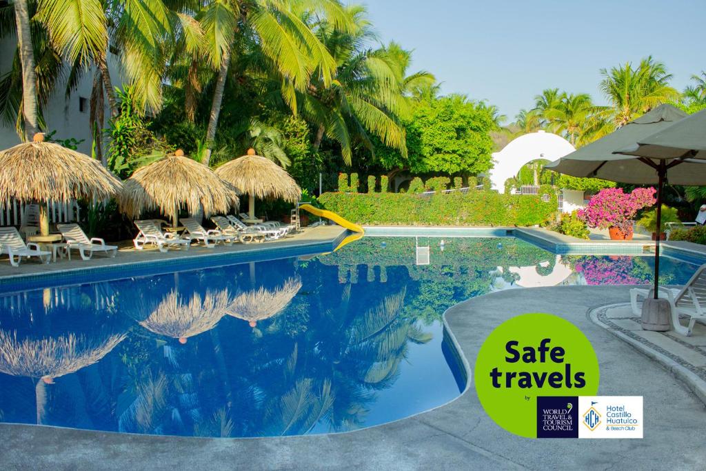 una piscina del complejo con un cartel que dice que viaje seguro en Hotel Castillo Huatulco & Beach Club, en Santa Cruz Huatulco