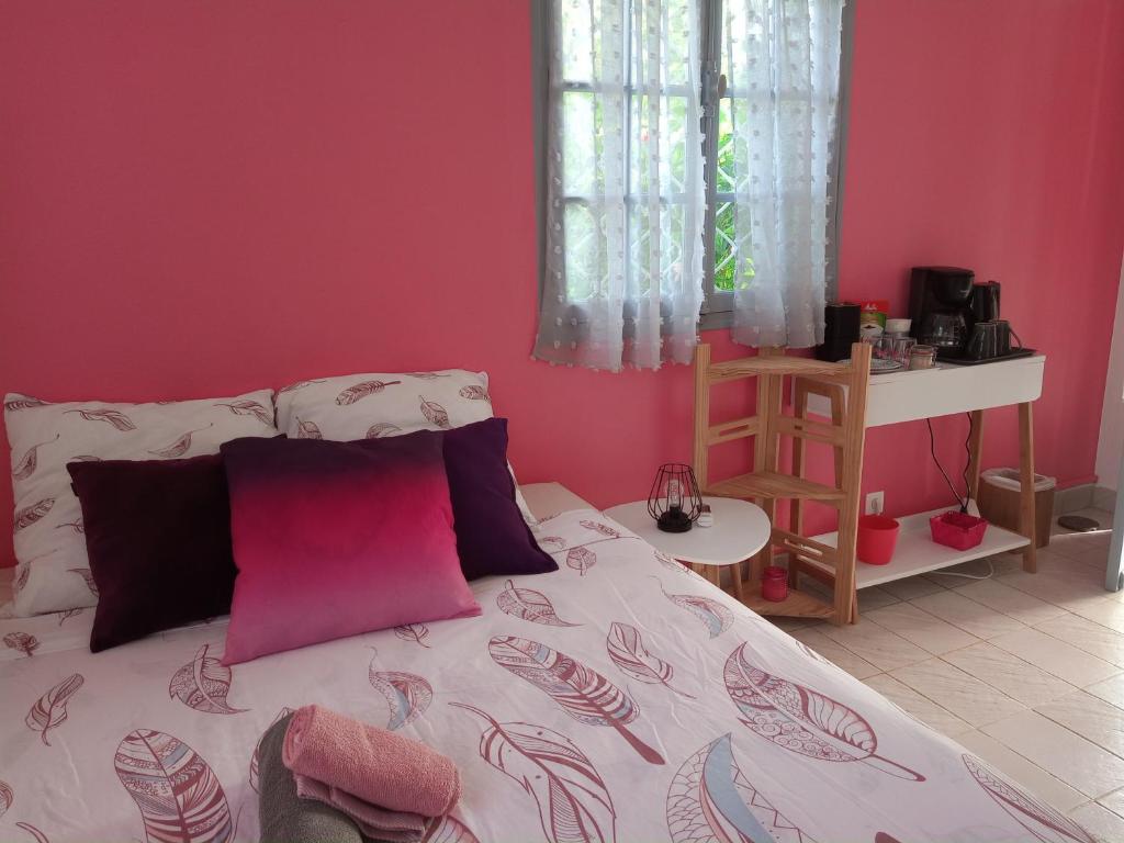 a bedroom with a bed with a pink wall at Jardin des Anges-Bungalows créoles et studio in Le Moule