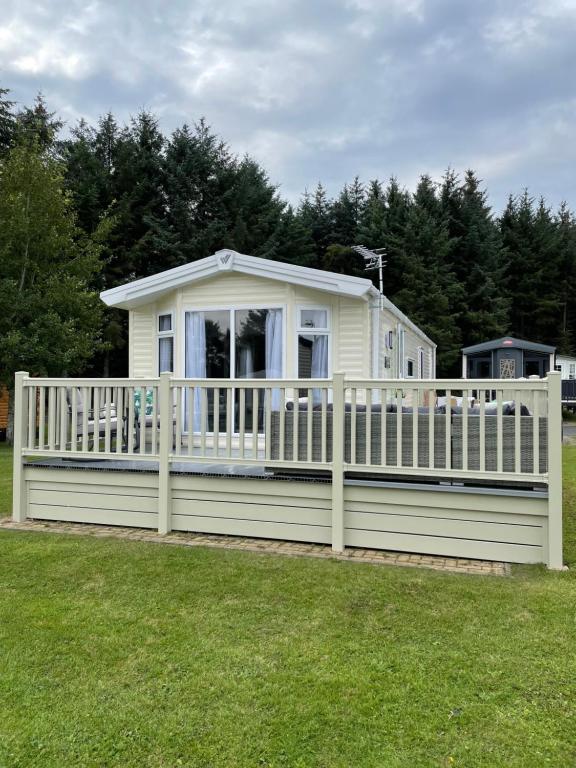 une maison avec une clôture blanche sur une cour dans l'établissement Lazy Bear Lodge Northumberland, à Swarland