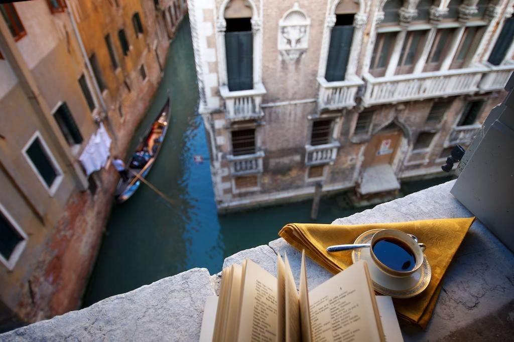 un livre et une tasse de café sur une corniche à côté d'un canal dans l'établissement CA FOSCARINI 1, à Venise