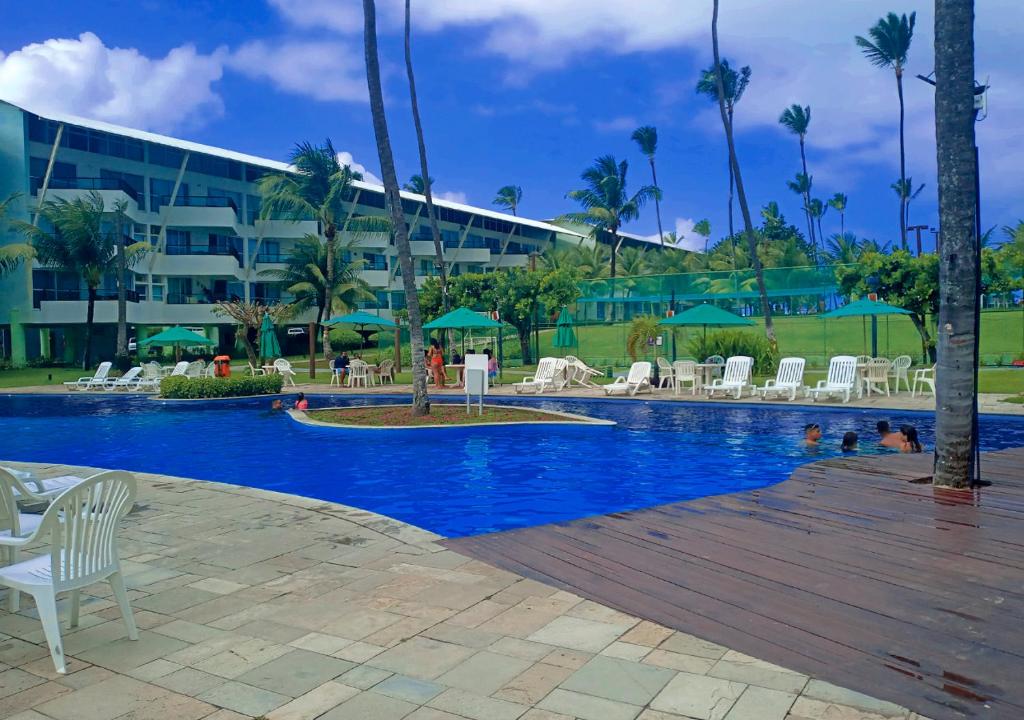 uma piscina num resort com cadeiras brancas e um edifício em Resort Ancorar Porto de Galinhas Flat 5305 em Porto de Galinhas