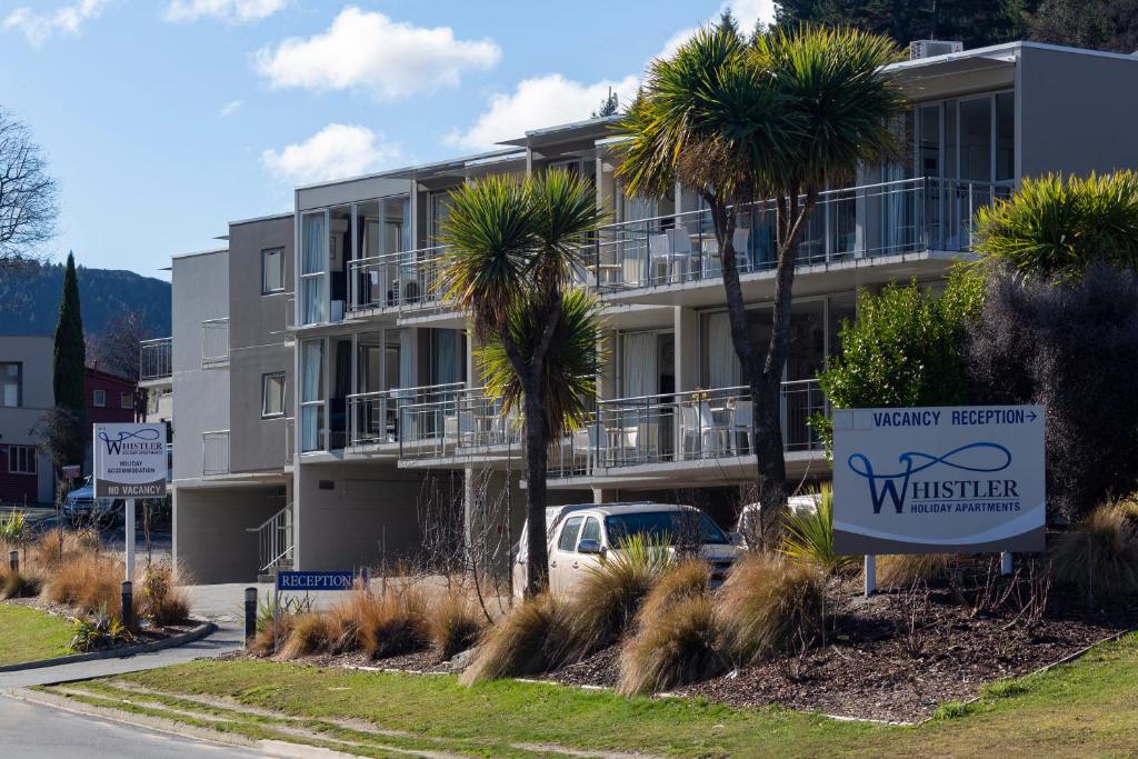 a building with palm trees and a sign in front of it at The Whistler Holiday Apartments in Queenstown