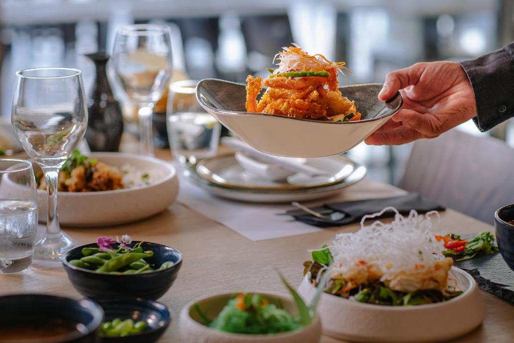 a person holding a bowl of food on a table at Ivi Mare - Designed for Adults by Louis Hotels in Paphos