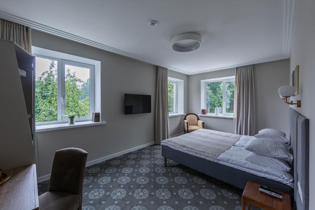 a bedroom with a bed and a chair and windows at Park Hotel Šiauliai in Šiauliai